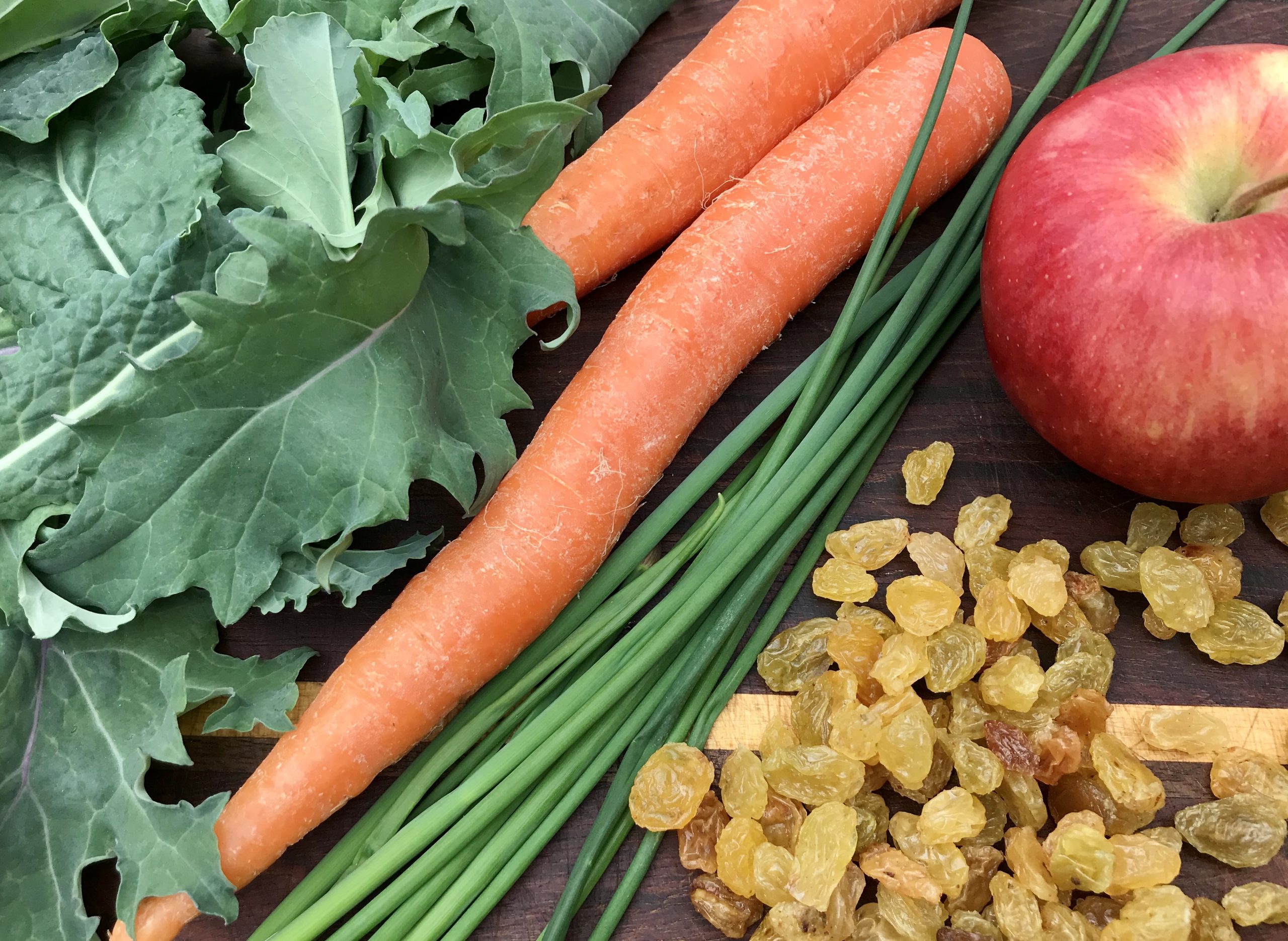 Kale, apple, carrots, raisins and chives on a cutting board
