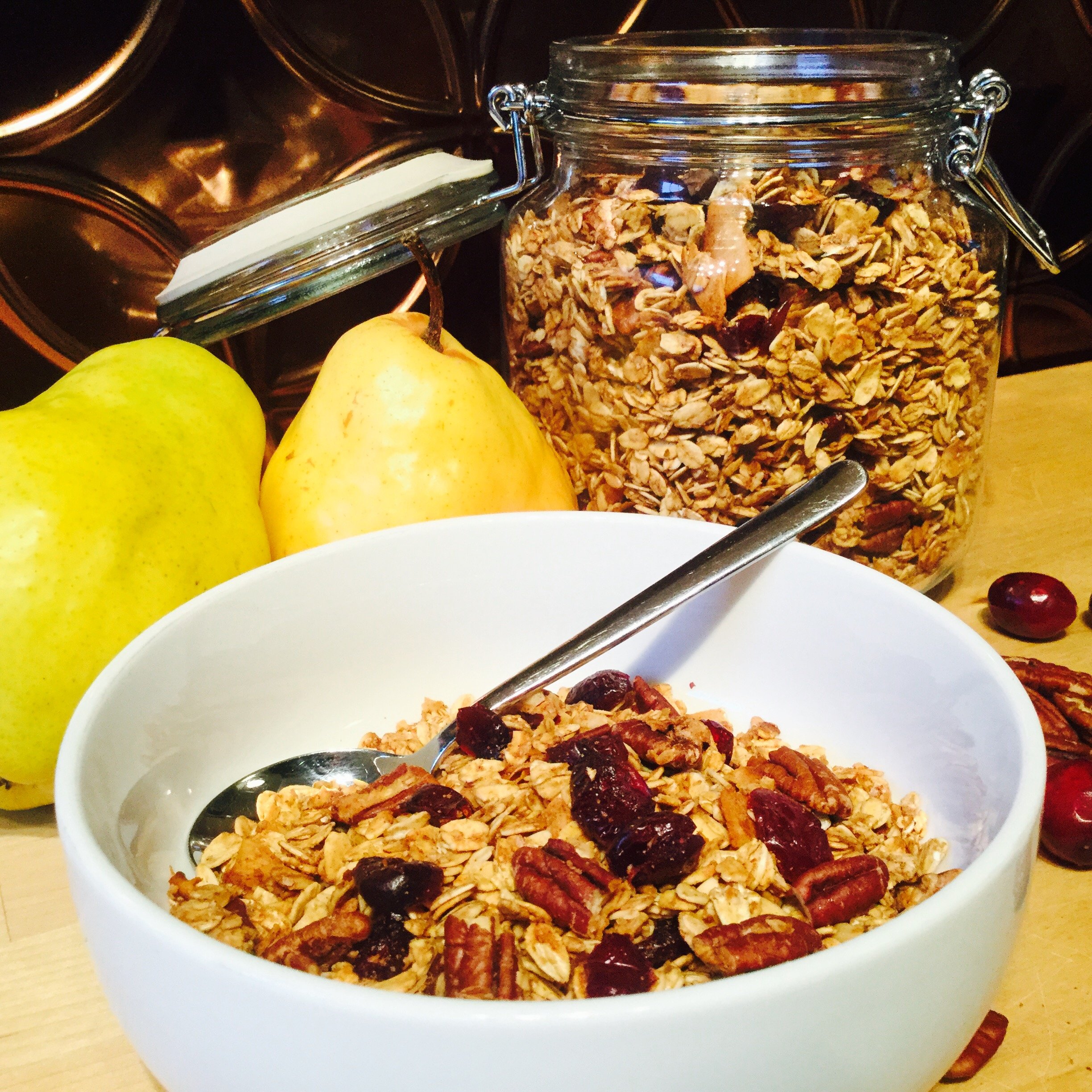 Bowl of granola with pears, pecans and cranberries, large container of granola in background